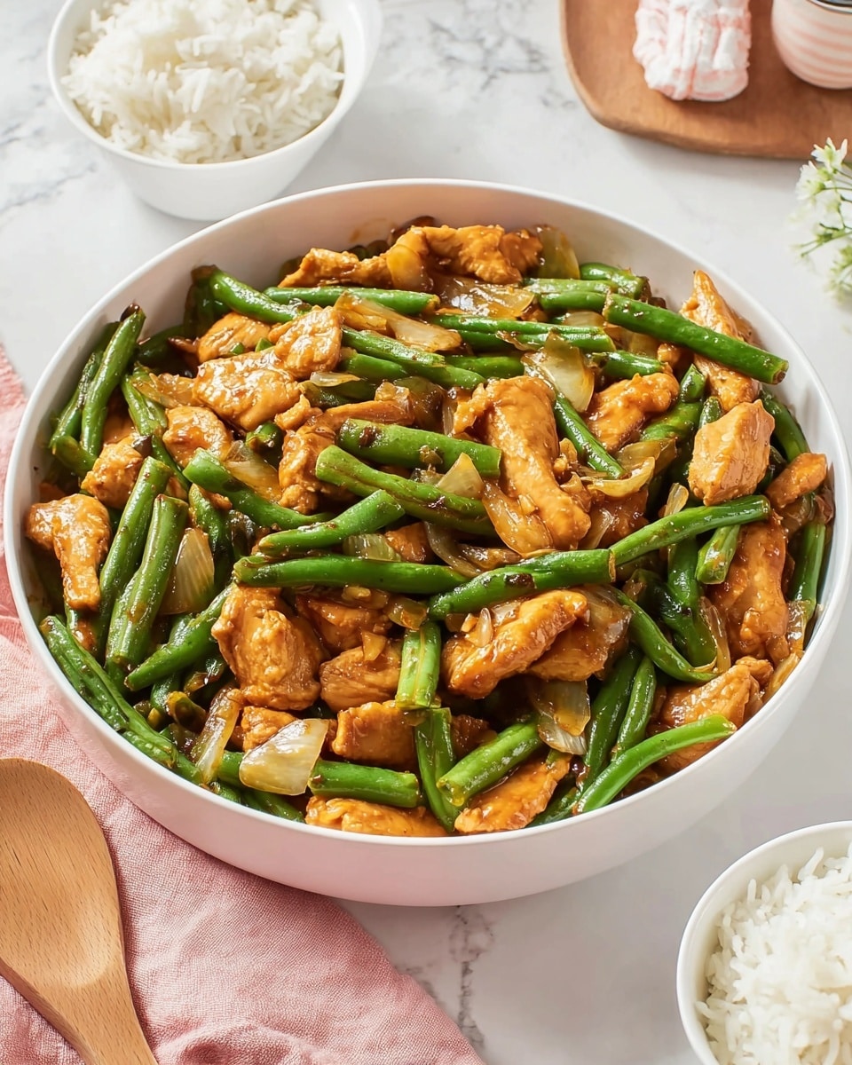 The dish shows a white bowl filled with three main layers: bright green cut green beans, medium-sized orange-brown chicken pieces coated with a shiny sauce, and scattered small chunks of light brown onions throughout. The green beans are cut into short pieces and mixed evenly with the chicken, giving a fresh, cooked look. The chicken pieces are smooth and soft-looking with light sauce glaze reflecting the light. Around the bowl, there are two white bowls with fluffy white rice grains. The background is a white marbled surface with a wooden utensil and a light pink cloth nearby, creating a clean and fresh setting. photo taken with an iphone --ar 4:5 --v 7