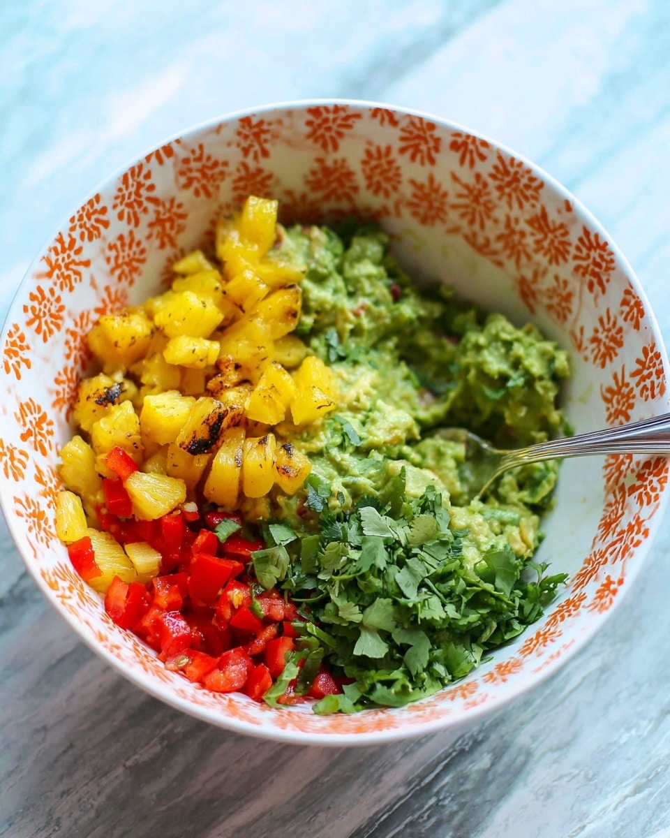 The image shows a white bowl with orange flower patterns on the inside edge, filled with four layers of fresh ingredients. The base layer is bright green mashed avocado spread unevenly inside the bowl. On top, there are small bright yellow grilled pineapple chunks on the left, finely chopped red bell pepper pieces in the top center, and a fresh green herb like chopped cilantro placed on the bottom right. A silver spoon is resting inside the bowl on the right side, partly buried in the mashed avocado. The bowl sits on a surface that looks like white marble. Photo taken with an iphone --ar 4:5 --v 7