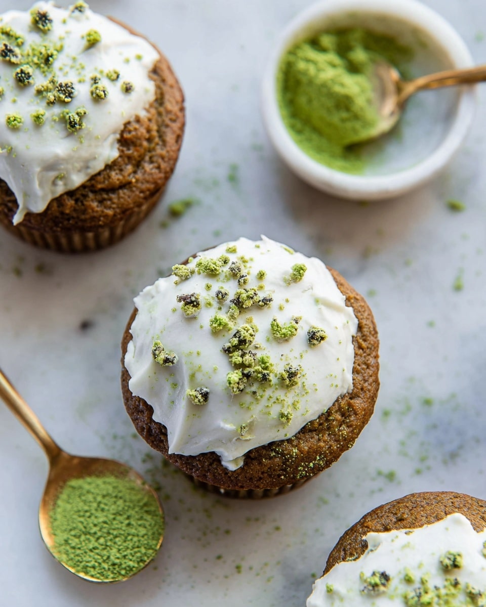 The image shows three muffins with two main layers each. The bottom layer is a brown muffin base with a slightly rough texture. On top of each muffin is a white frosting layer that is unevenly spread and sprinkled with small green powder bits, adding a pop of color. The muffins sit on a white marbled surface, and to the side, there is a white bowl with green powder and a small golden spoon inside. Some of the green powder is scattered around the muffins. Photo taken with an iphone --ar 4:5 --v 7