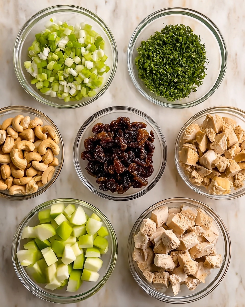 Seven clear glass bowls are arranged on a white marbled surface. The top left bowl holds chopped green onions, small round green and white pieces. The top right bowl contains finely chopped green herbs with a soft texture. At the center is a bowl filled with dark brown raisins, wrinkled and shiny. To the left middle, a bowl is full of whole cashew nuts, light brown and curved. On the right middle is a bowl filled with small diced light green celery pieces. The bottom left bowl has small diced green apple pieces, fresh with a mix of light green and white. The bottom right bowl contains cubed, lightly peppered cooked chicken pieces, light beige in color with a firm texture. photo taken with an iphone --ar 4:5 --v 7