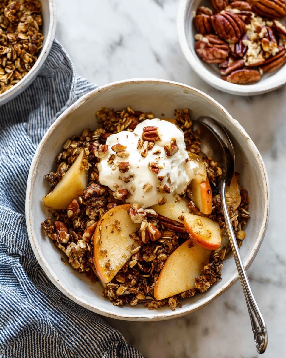 A white bowl filled with sliced apples at the bottom, covered by a thick layer of toasted oats mixed with chopped pecans, giving a crunchy texture and dark brown color. On top, a scoop of white cream is placed, sprinkled with small pecan pieces. A silver spoon rests inside the bowl, and nearby is a white bowl with more chopped pecans. The bowls are set on a white marbled surface with a blue and white striped cloth next to them. photo taken with an iphone --ar 4:5 --v 7