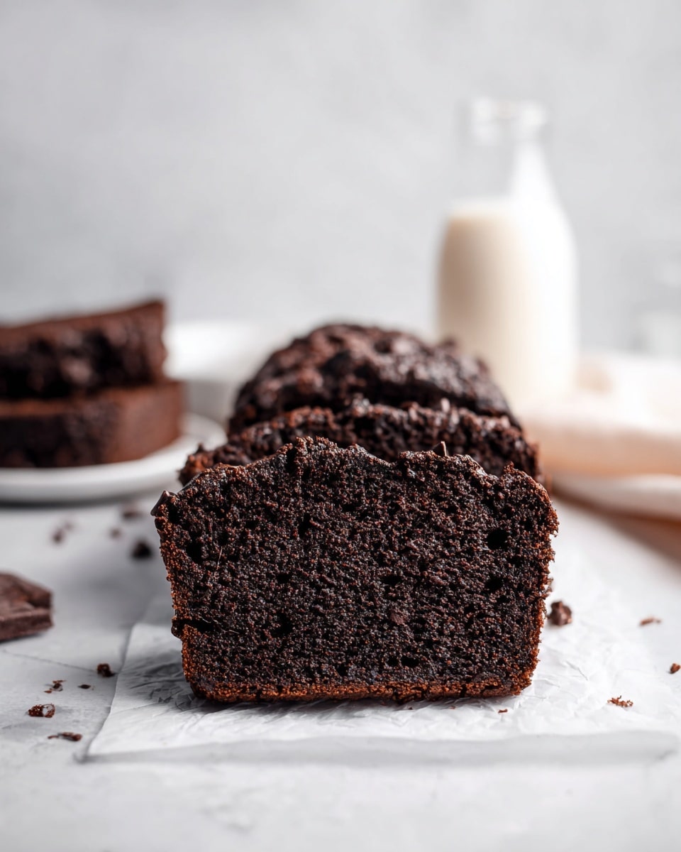 The image shows a close-up of two thick slices of dark chocolate bread, placed on a piece of white parchment paper on a white marbled surface. The bread has a moist, crumbly texture with small chocolate chips embedded throughout. Behind the slices, there are blurred chocolate bread pieces on white plates and a glass bottle filled with milk. The focus is mainly on the front bread slices, highlighting their rich, deep brown color and soft texture. Photo taken with an iphone --ar 4:5 --v 7